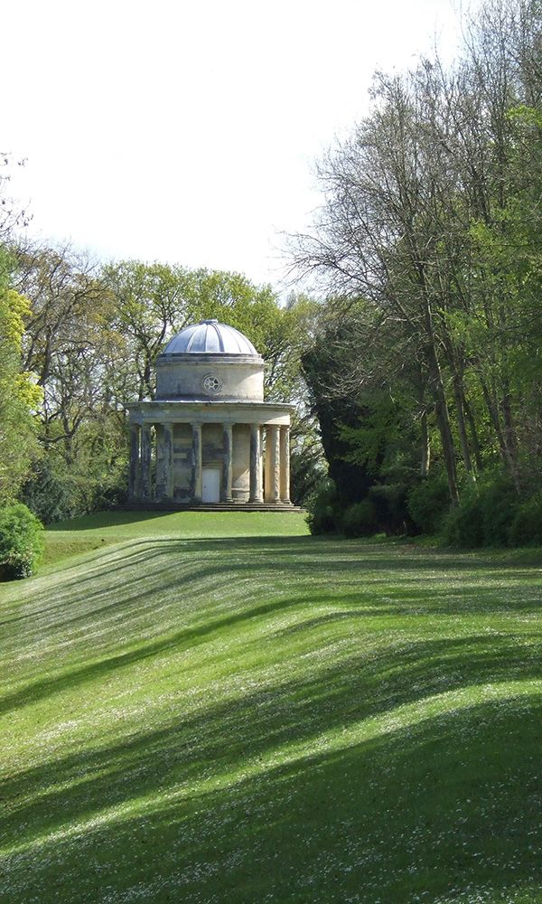 A classical-style rotunda stands at the end of a banked grass promenade lined by trees.