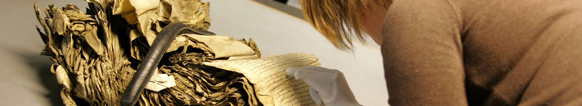A female archivist wears protective gloves to examine old manuscript records.