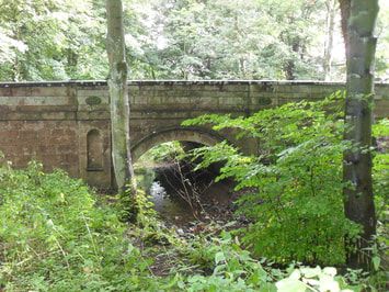 Stone bridge crossing narrow stream in woodland