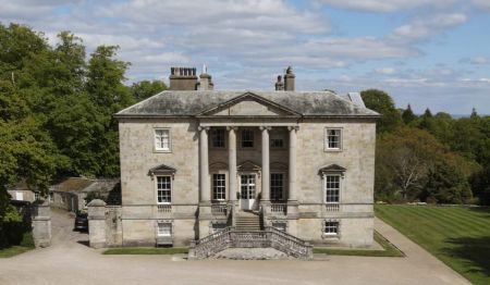 Photograph of country house with steps up to entrance and woodland behind