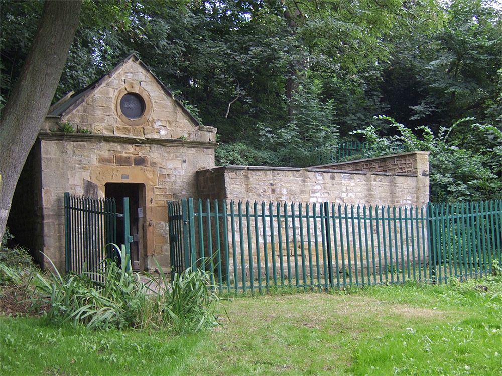 A stone-built structure surrounded by trees and a metal fence.