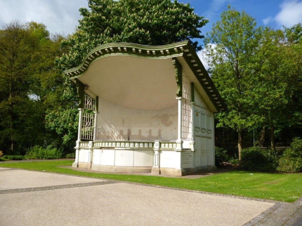 A white wooden enclosure with a green canopy is surrounded by grass with a path in the foreground.