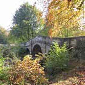 A large stone bridge over a river surrounded by trees with autumn colours.