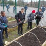 School children hold netting to cover recently-planted raised beds.